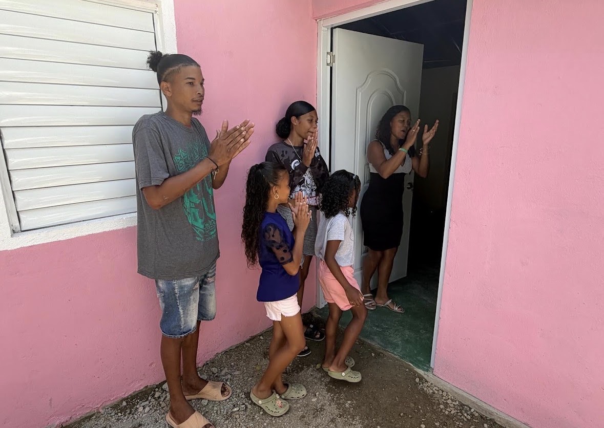 Family receiving keys — standing outside their new pink home