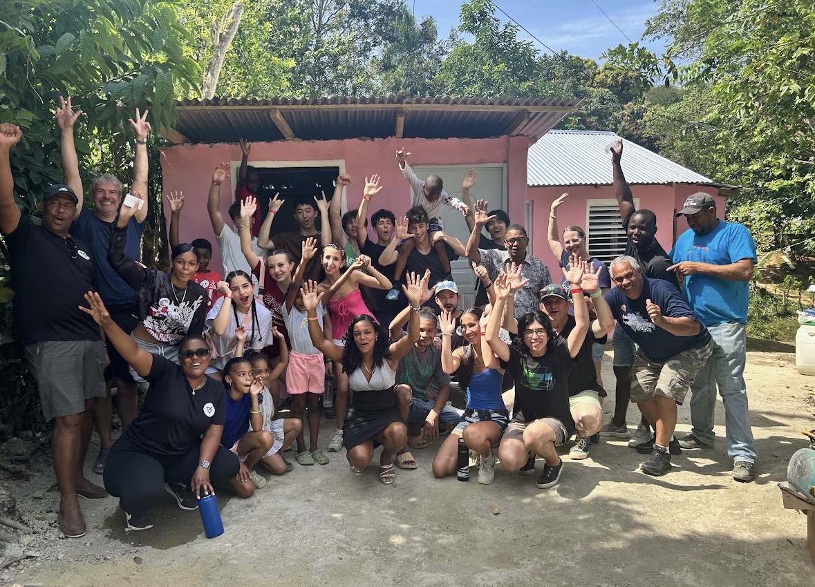 Volunteer team portrait — group celebrating in front of a completed home